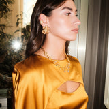 Woman wearing a mustard yellow satin dress with cut-out design, gold earrings, and necklace.
